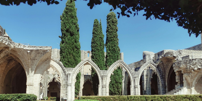 Bellapais Manastırı’nın tarihi kemerleri ve uzun servi ağaçlarıyla çevrili huzur dolu avlusu görülüyor.